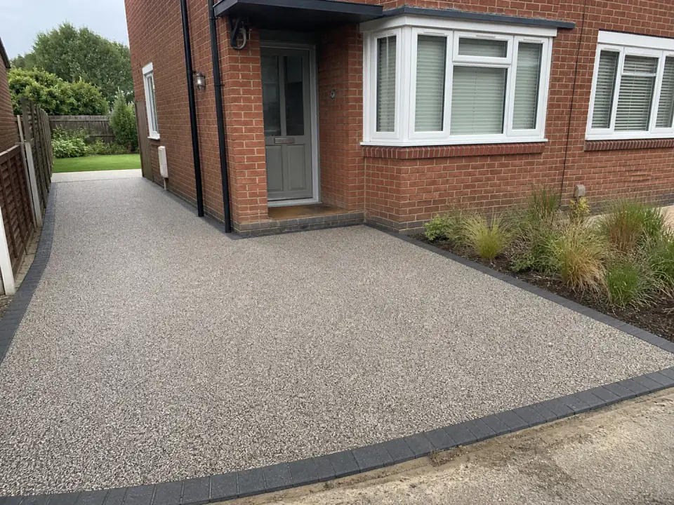 Warm-grey resin-bound driveway with charcoal edging at a red-brick UK home